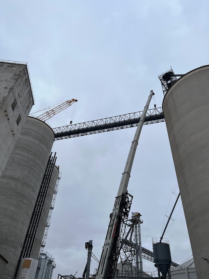 Slipform concrete grain storage silos under construction, featuring a crane and above-ground reclaim tunnels for grain handling efficiency.