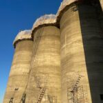 Concrete silos of the Holcomb Grain Facility, showcasing high-capacity storage design and construction scaffolding against a clear blue sky.