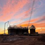 Holcomb Grain Facility construction site featuring a 92-foot-tall concrete structure under sunset sky, showcasing rail loadout tunnel and construction activities for high-capacity grain handling.
