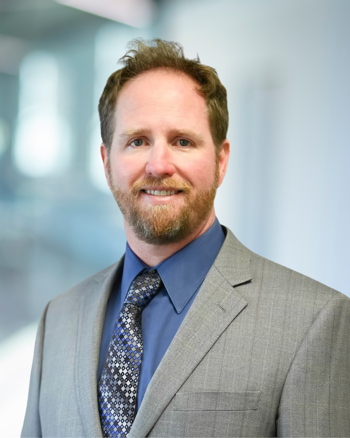 Chris Heiser, Senior Engineer at KC Engineering, wearing a gray suit and blue shirt, smiling against a blurred professional background.