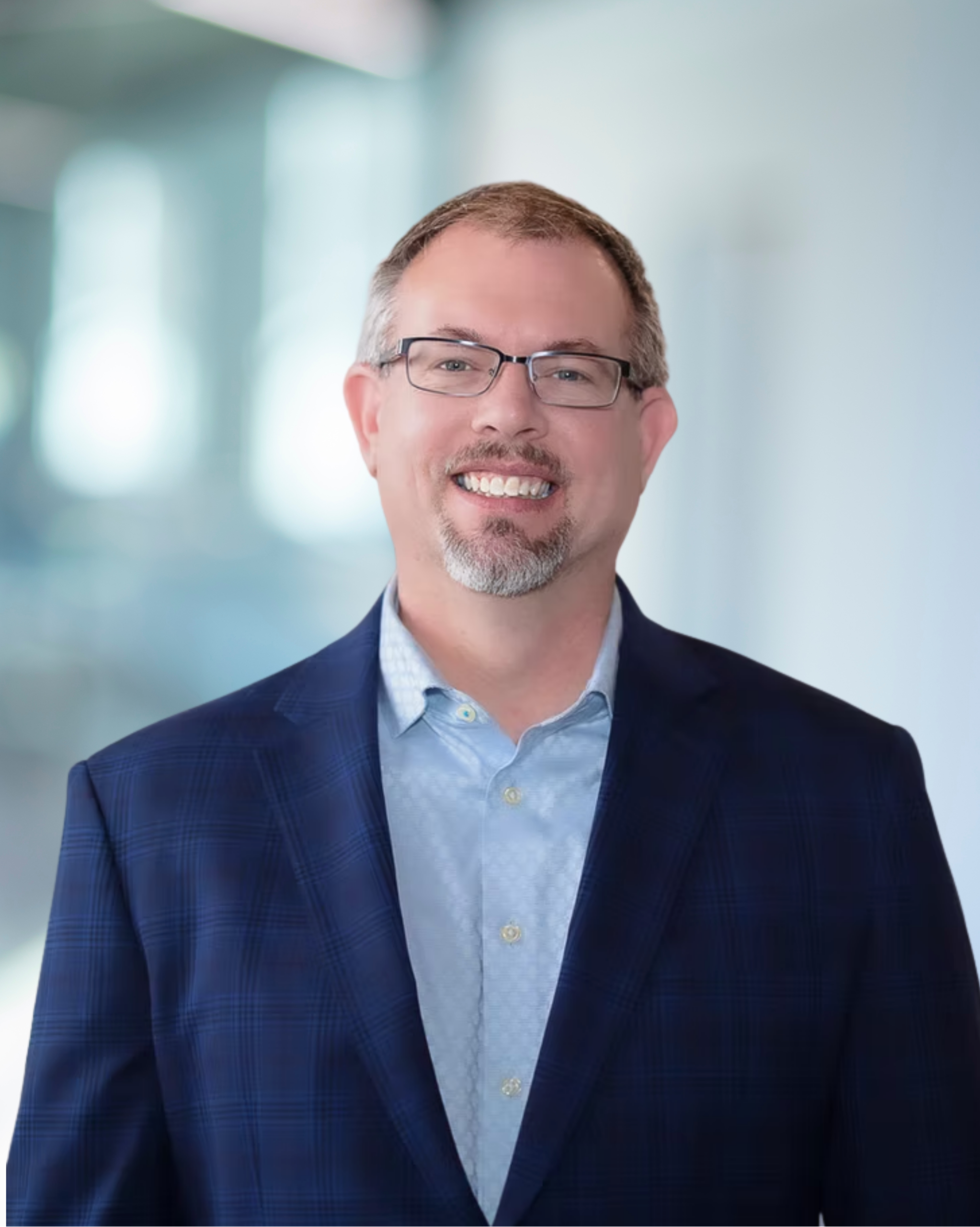 Eric Hanson, Principal and President of KC Engineering, smiling in a professional setting, wearing a blue plaid blazer and light blue shirt, representing the leadership team committed to innovative engineering solutions.