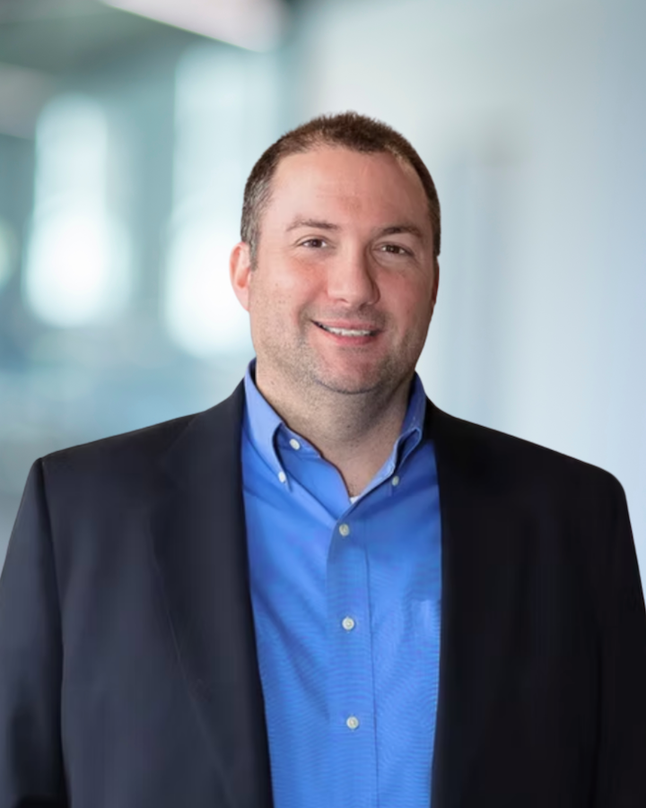 Jason O'Mara, Principal and Vice President at KC Engineering, smiling in a professional setting, wearing a blue shirt and black blazer, with a blurred office background.