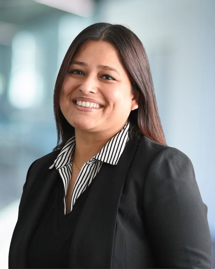 Rina Thapa, smiling CAD Technician at KC Engineering, wearing a black blazer with a striped shirt, professional setting.