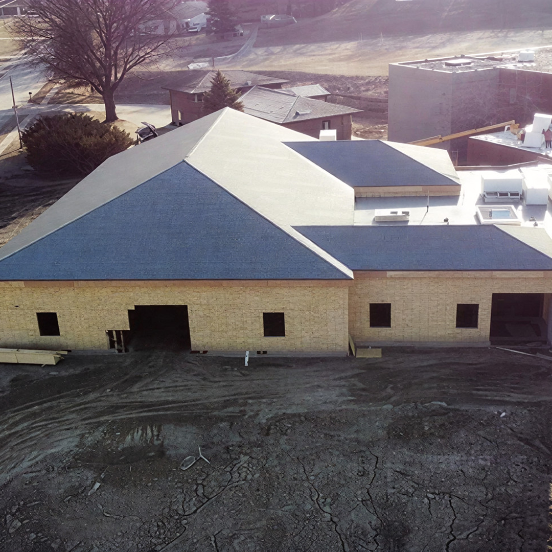 Newly constructed building with a pitched roof and partially finished exterior, surrounded by a construction site, reflecting KC Engineering's architectural design services for institutional projects.