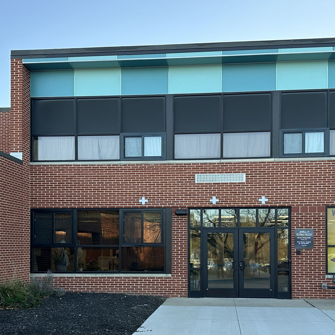 Modern brick building facade with large windows, showcasing a blend of architectural design elements, featuring a prominent entrance and decorative crosses, emphasizing code-compliant and functional design in institutional facilities.