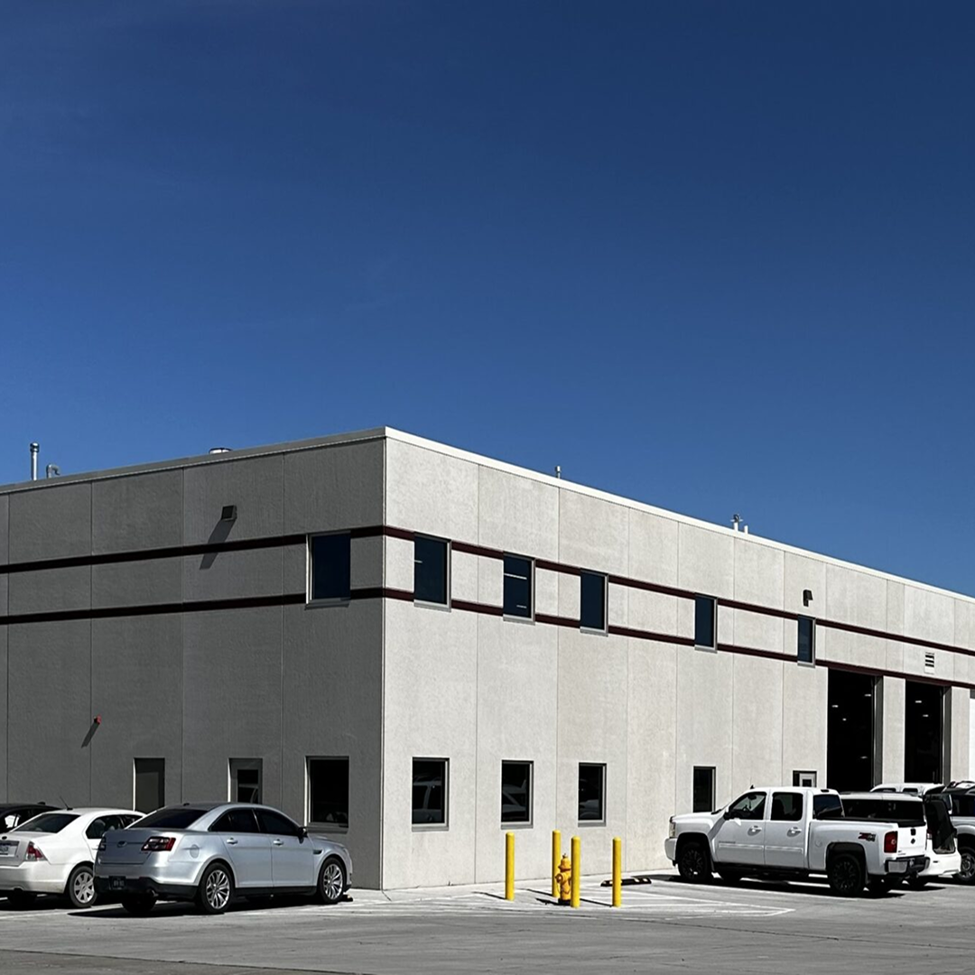 Modern industrial building with large windows and a gray exterior, showcasing parking area with various vehicles, emphasizing KC Engineering's architectural design capabilities for commercial facilities.