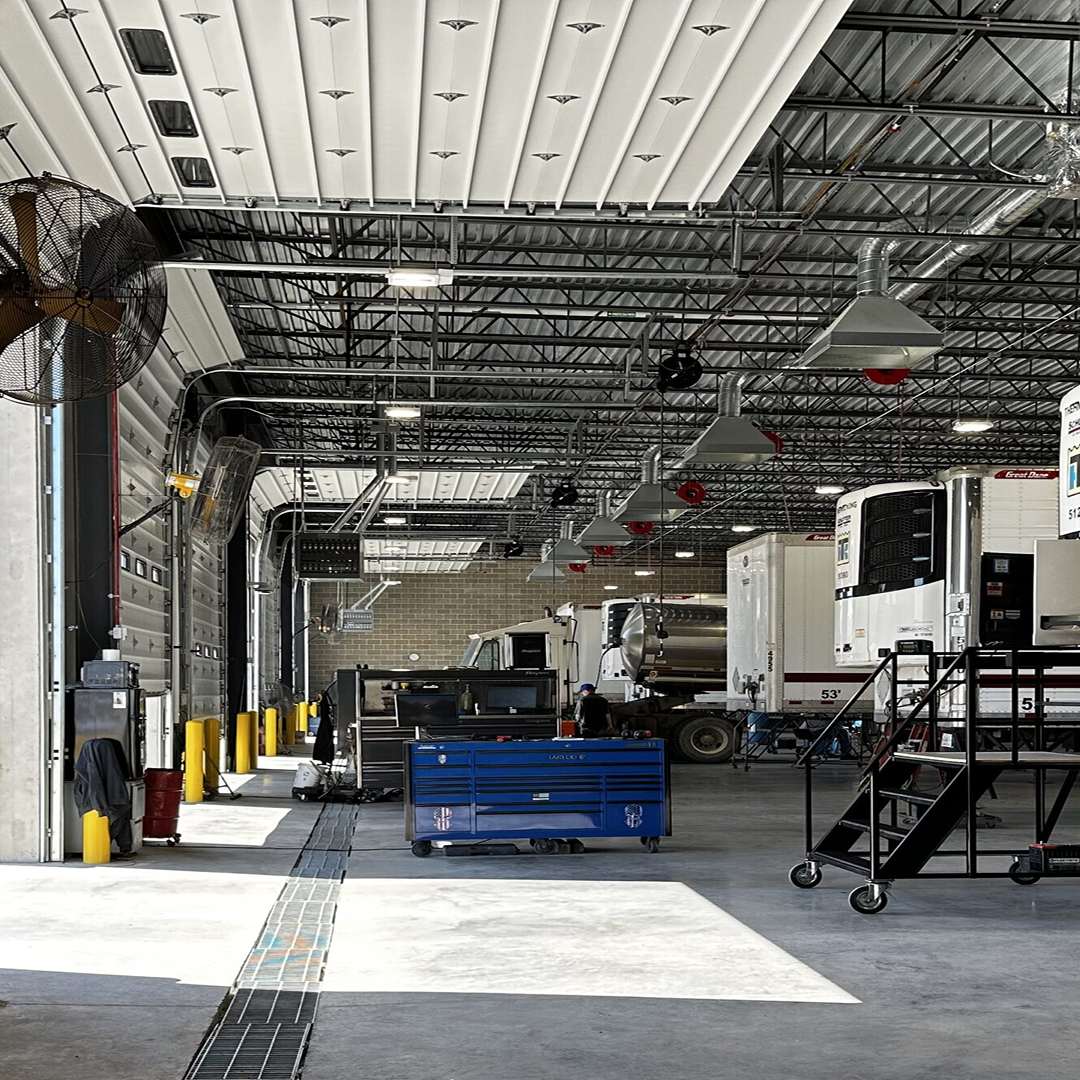 Interior of a commercial garage with large trucks, tool storage, ventilation systems, and safety features, emphasizing practical design for efficiency and functionality in architectural projects.