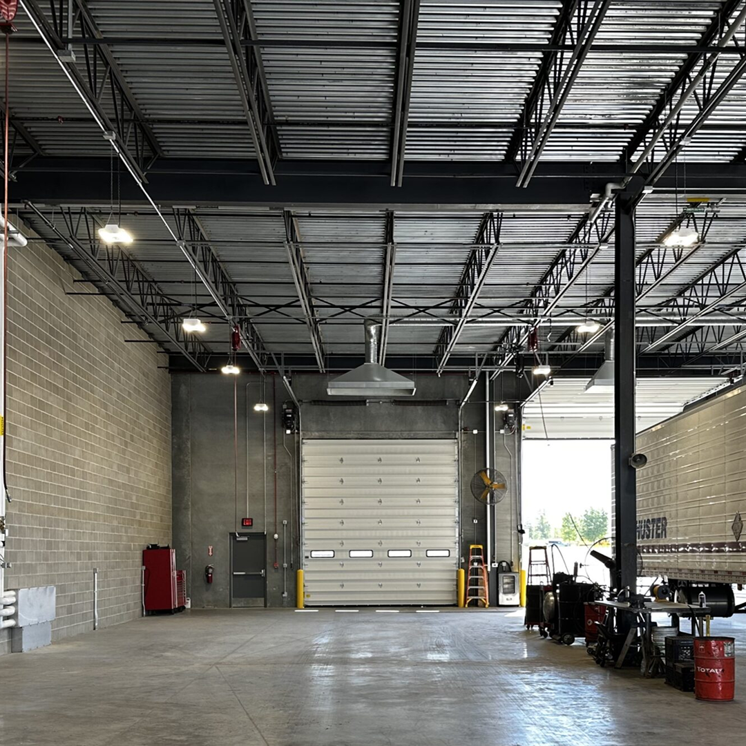 Spacious industrial facility interior with high ceilings, overhead lighting, large roll-up door, and equipment for operational efficiency, reflecting KC Engineering's focus on practical architectural design.