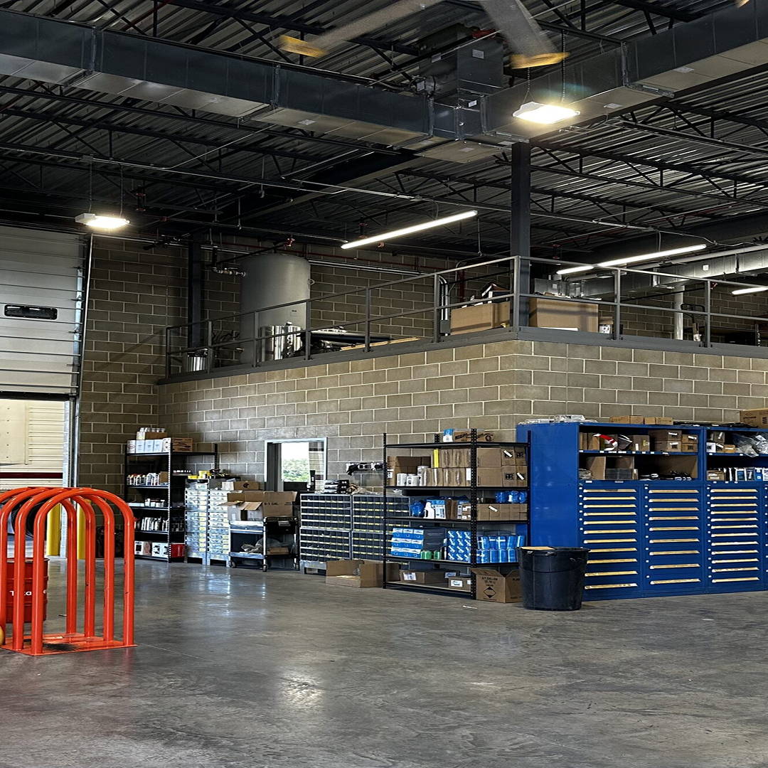 Interior view of a well-organized industrial workspace featuring storage shelves with tools and materials, a large metal tank on an upper level, and red safety barriers, emphasizing efficient planning and structural feasibility in architectural design.