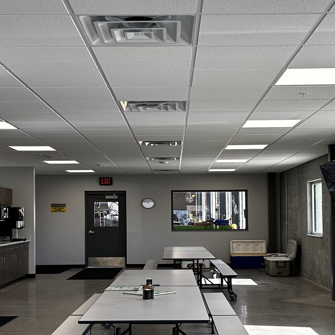 Interior of a functional workspace featuring tables, a coffee station, and a clock, with overhead lighting and a door leading outside, reflecting KC Engineering's commitment to practical design in architectural environments.