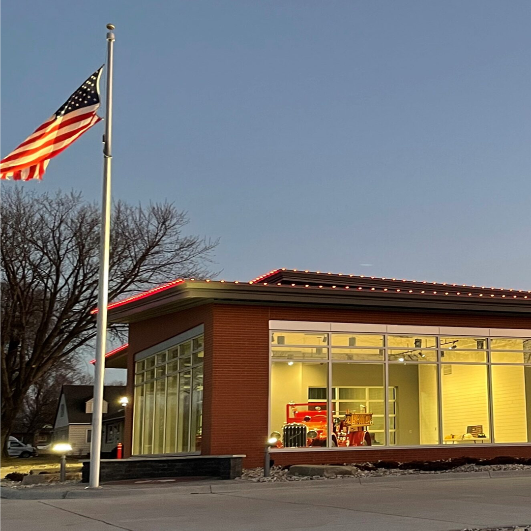 Sioux Center Fire Station exterior at dusk, featuring an American flag, modern architectural design, large glass windows, and visible fire truck inside, highlighting KC Engineering's focus on practical and code-compliant facility design.
