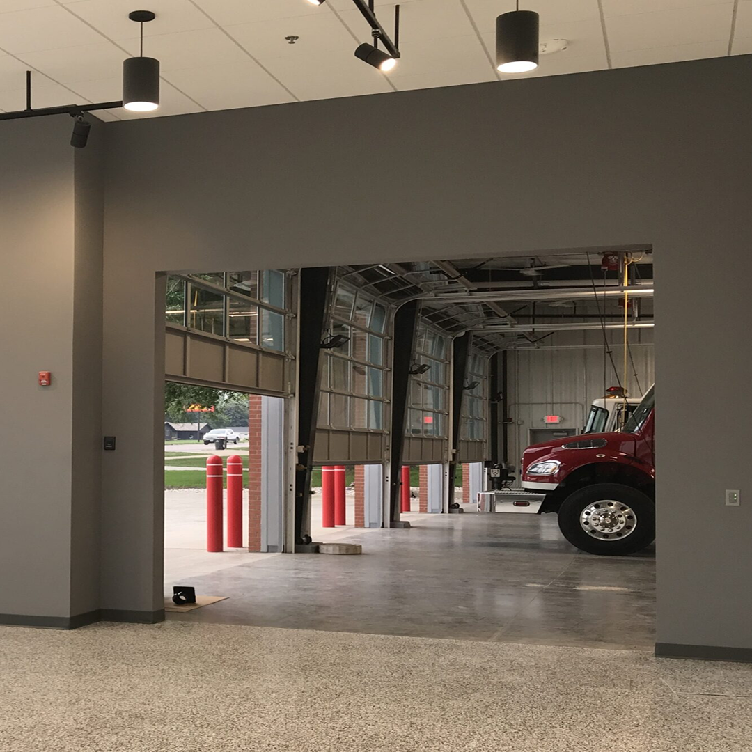 Interior view of Sioux Center Fire Station showing open garage doors, red fire truck partially visible, and safety bollards, emphasizing architectural design for functionality and accessibility.