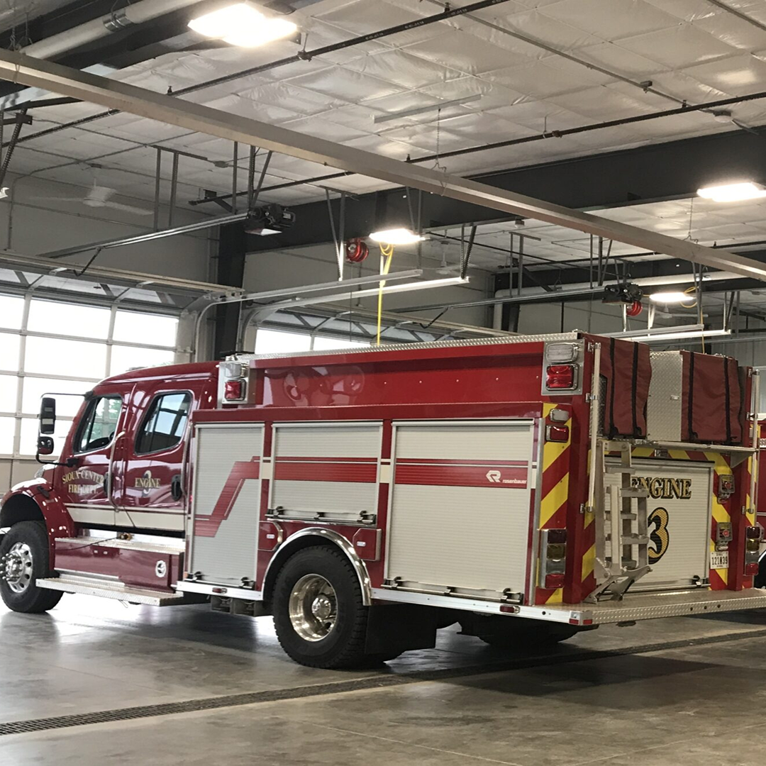 Red fire truck labeled "Engine 3" parked inside a modern fire station, showcasing structural design elements relevant to architectural efficiency and safety in community facilities.