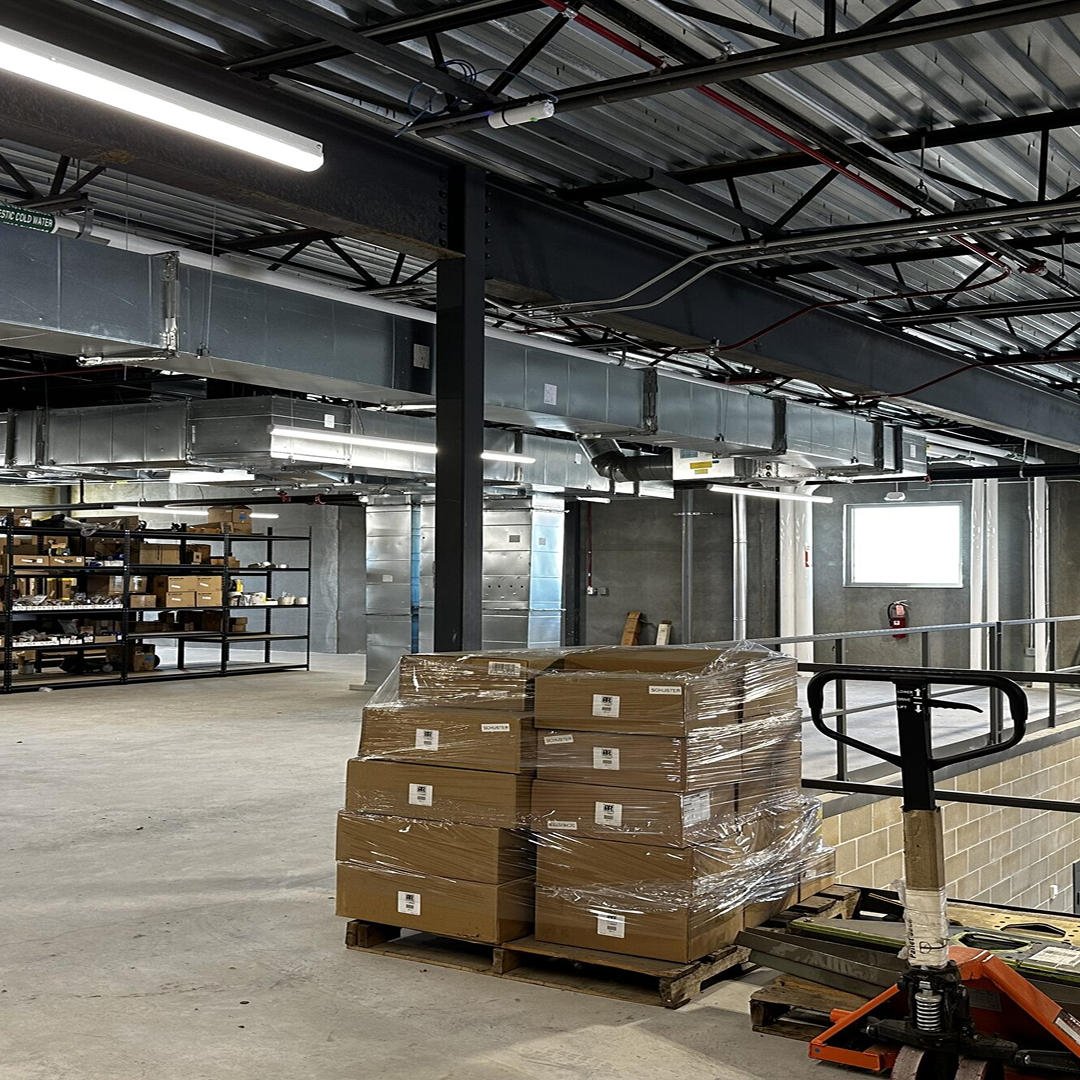Interior view of a construction site featuring stacked cardboard boxes on a pallet, shelving units with supplies, and visible ductwork, illustrating the practical design and organizational aspects of architectural projects by KC Engineering.
