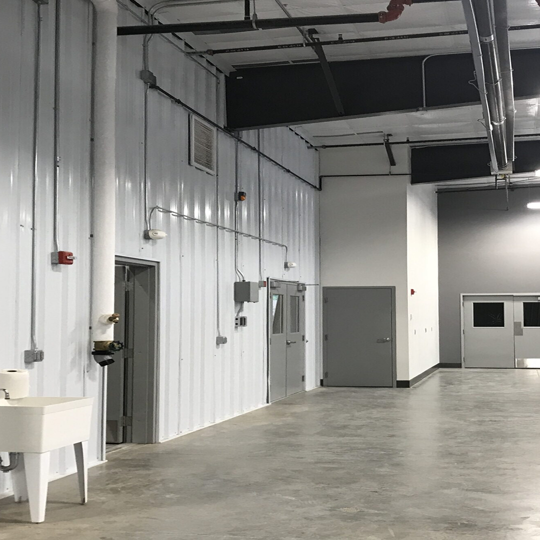 Interior view of a modern facility featuring metal panel walls, utility connections, a sink, and multiple doors, emphasizing practical design for architectural efficiency and code compliance.