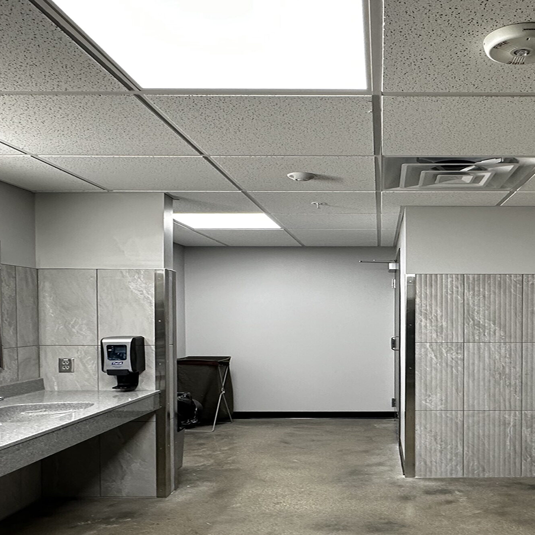 Modern restroom interior featuring gray walls, a marble sink countertop, a soap dispenser, and a partially visible door leading to a private stall.