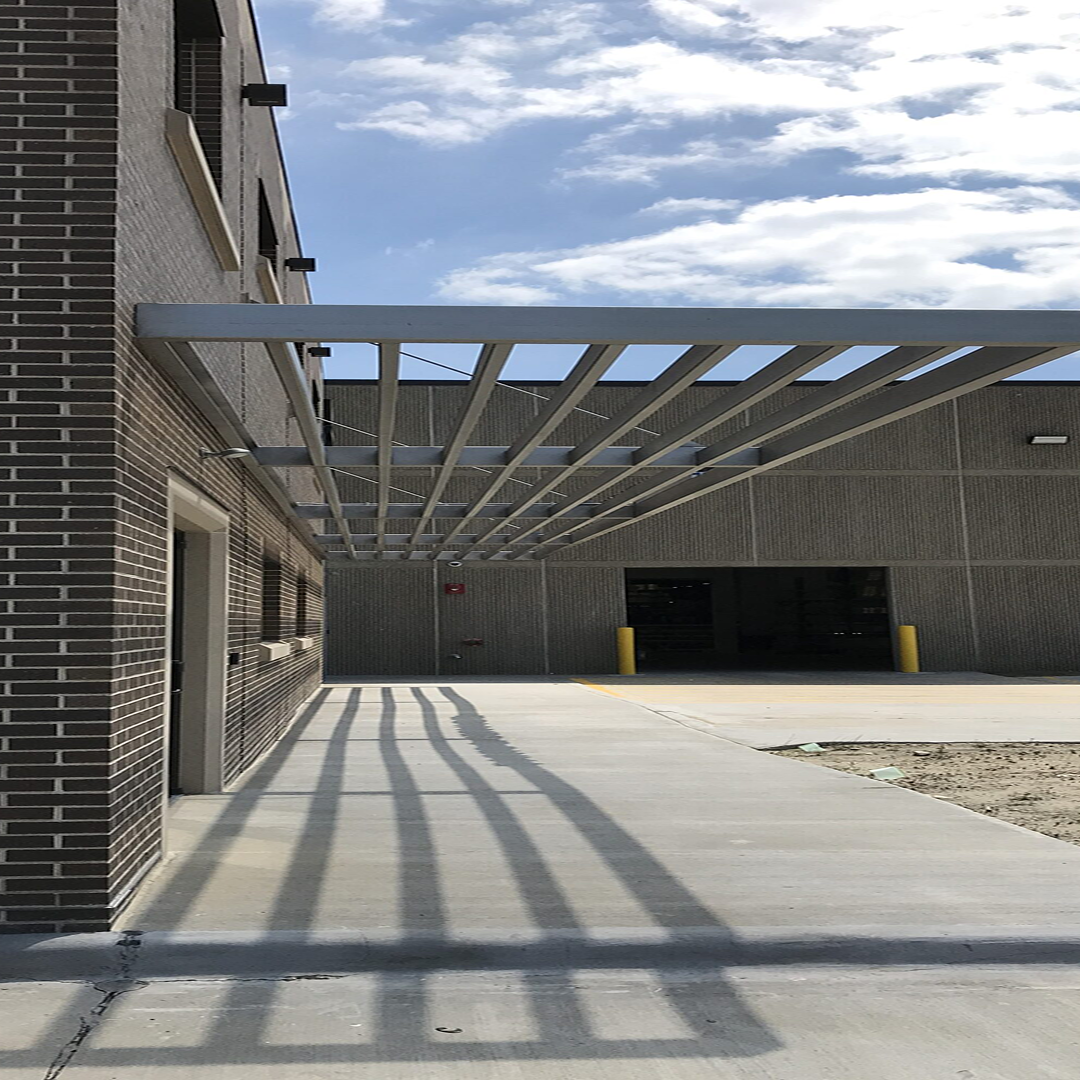 Architectural design featuring a modern building facade with a slatted overhang, concrete walkway, and industrial setting, emphasizing structural feasibility and project efficiency in construction.