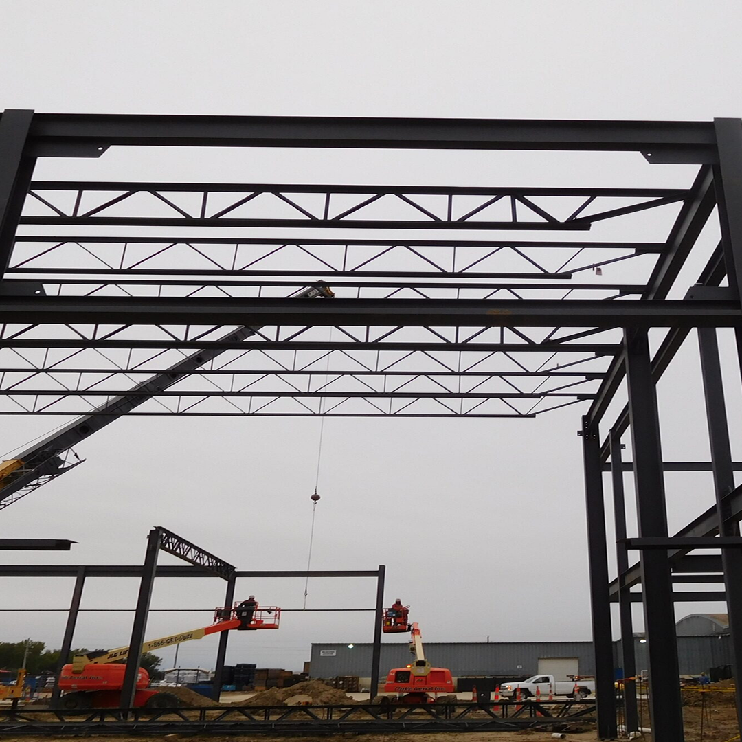 Construction site featuring steel framework assembly, cranes lifting structural elements, and workers in aerial lifts, illustrating KC Engineering's expertise in practical and code-compliant architectural solutions.