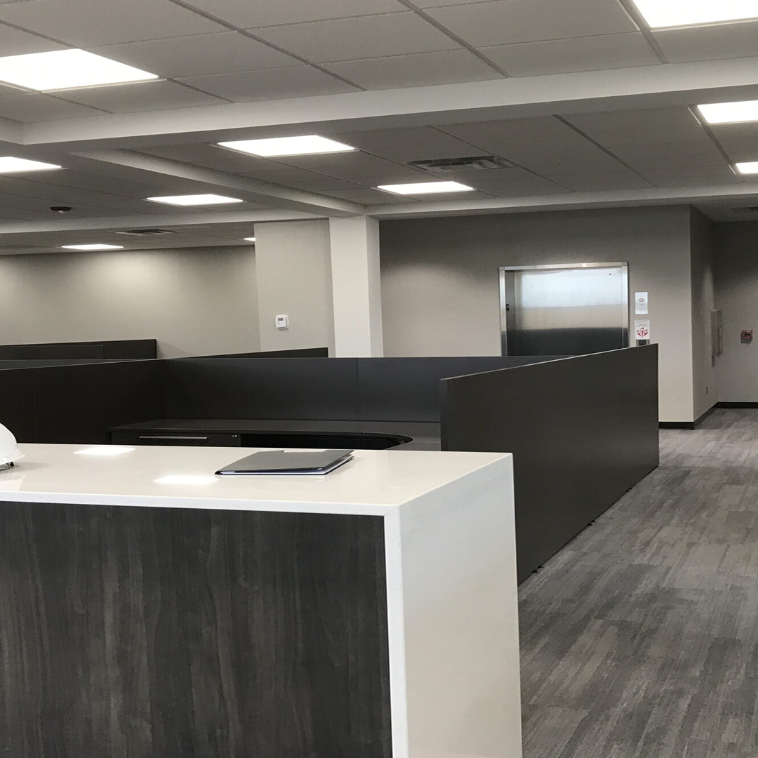 Modern office interior with cubicles, a reception desk, and elevator access, reflecting efficient architectural design and workspace planning.